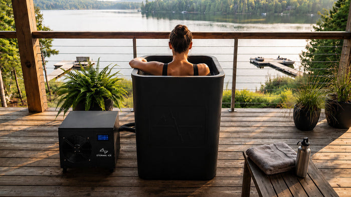 Woman in a water filled Eternal Ice Bath cold plunge tub beside the Power Chiller on a lakeside deck