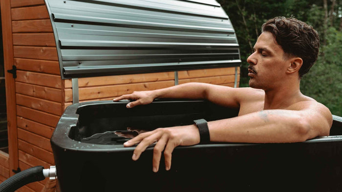 Man sitting in an Eternal Ice HD Ultimate insulated ice bath on a wooden deck, lid open, chiller hose connected.